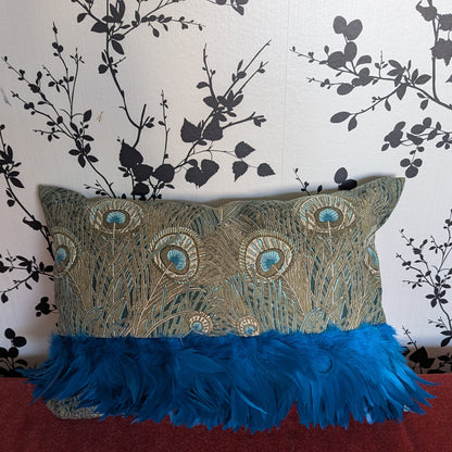 Decorative pillow with peacock feather design on a red surface against a floral wallpaper background